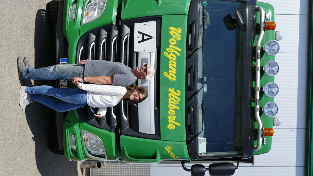 Zwei Personen stehen Rücken an Rücken vor einem grünen Lastwagen mit der Aufschrift „Wolfgang Häberle“.